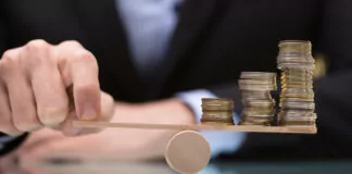 Businessperson Balancing Stacked Coins On Seesaw