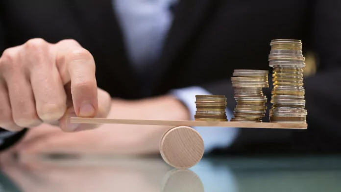 Businessperson Balancing Stacked Coins On Seesaw